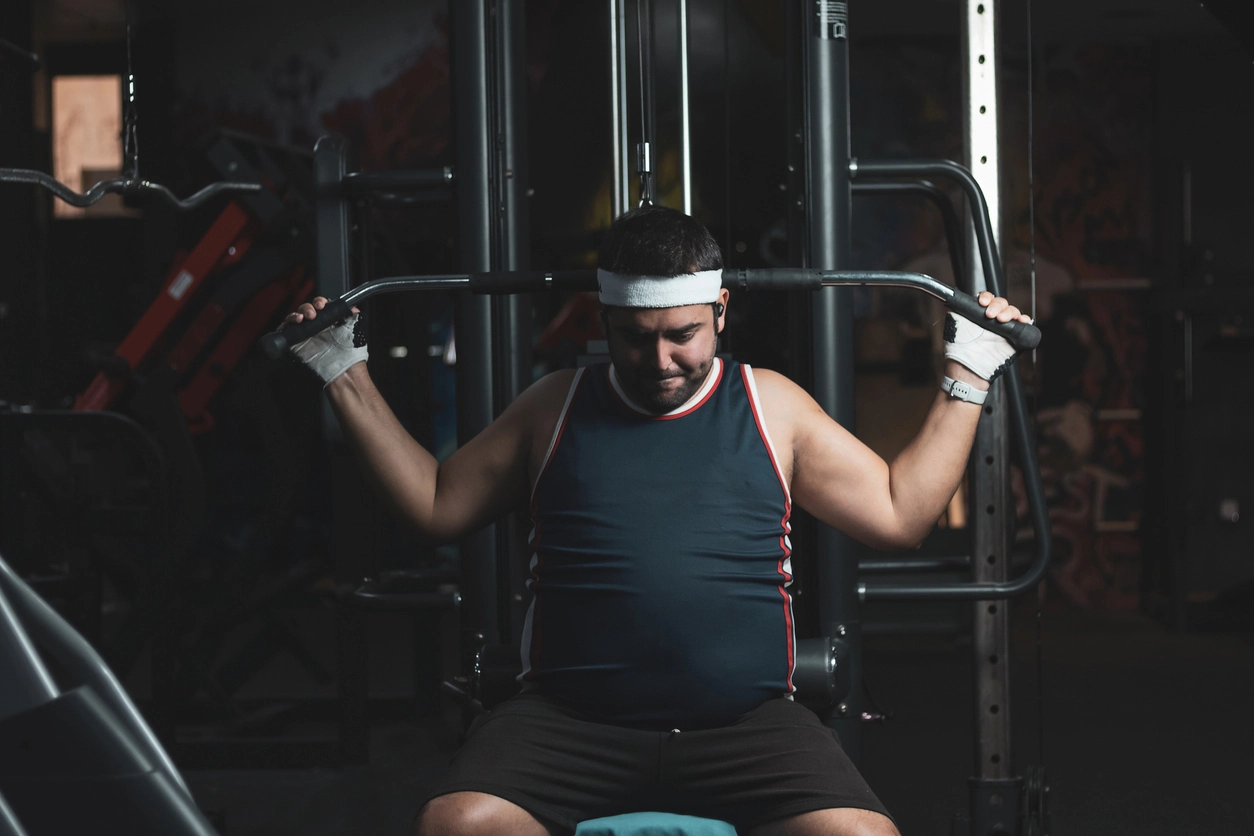 A funny chubby young man training inside a gym. Concept of effort and improvement.
